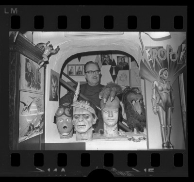 Forrest J. Ackerman, posing with monster masks and science fiction artwork in his Los Angeles, Calif. Home, 1969